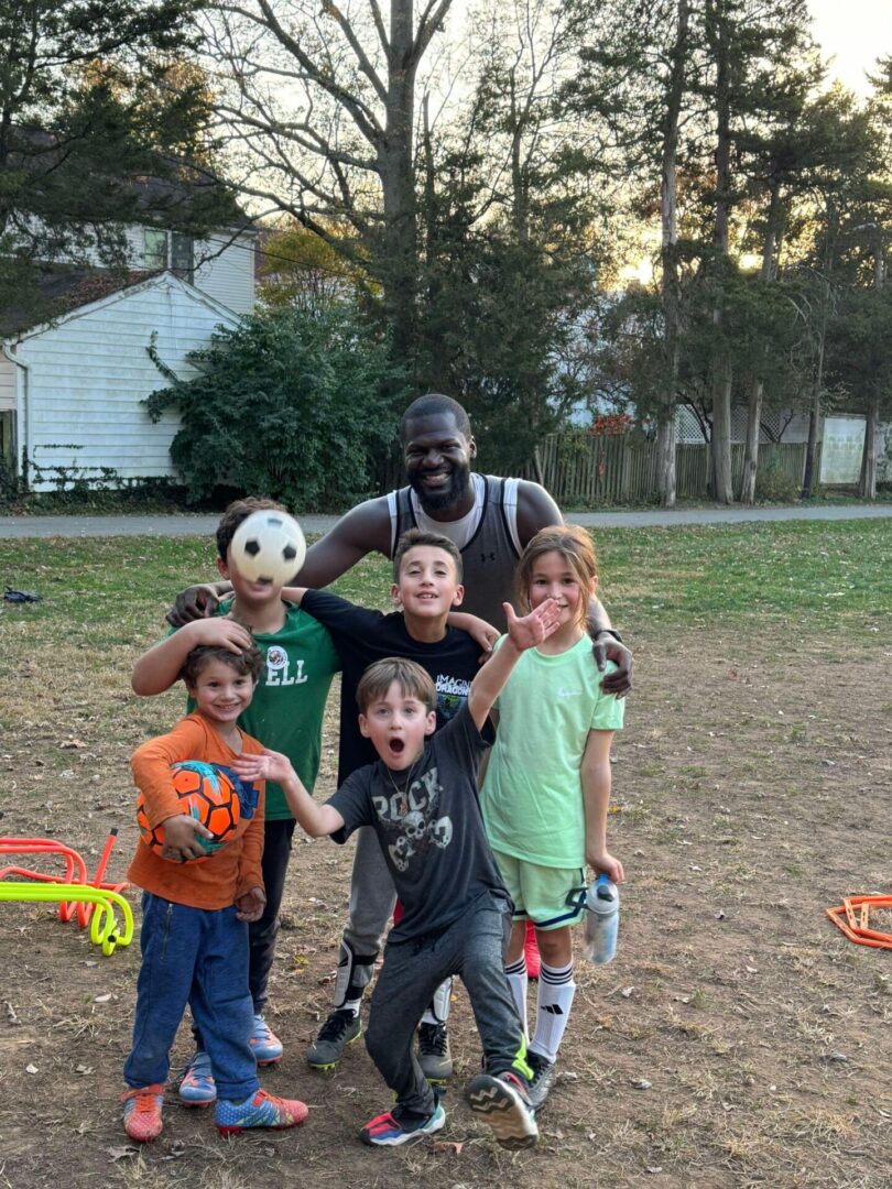 A man poses with a group of smiling children for a cheerful group photo outdoors.
